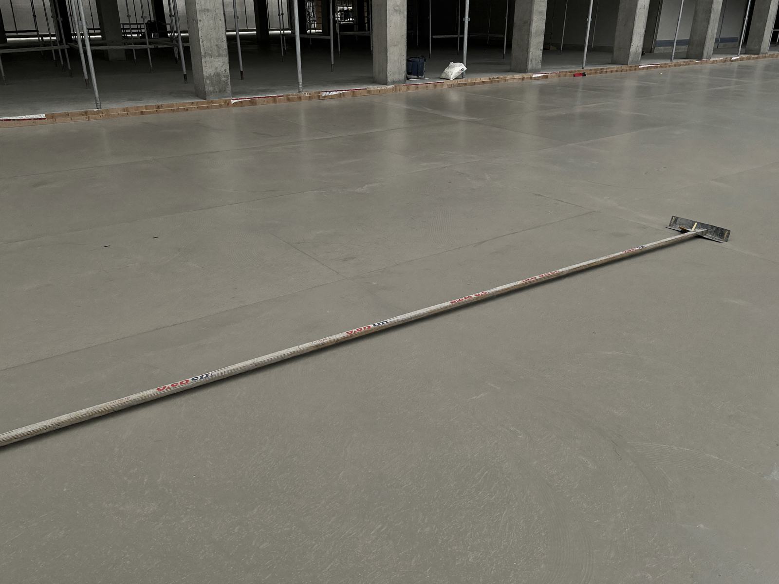 Large finished concrete floor slab with a bull float resting on the surface, columns and props beyond